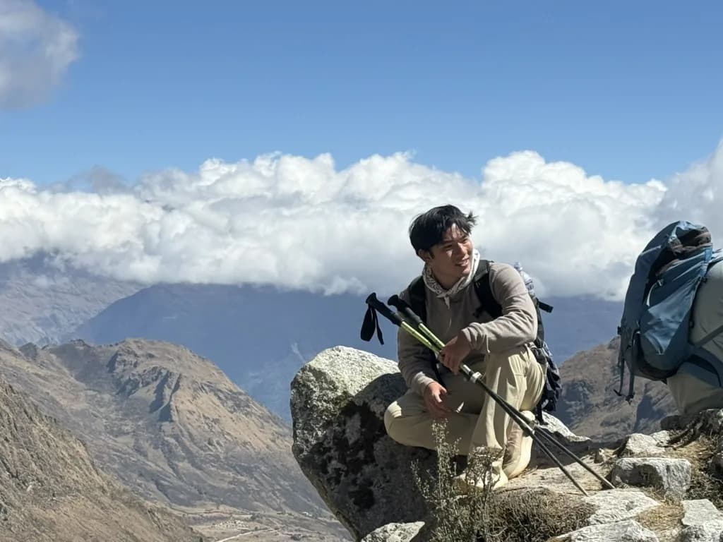 Zach sitting on a rock with trekking poles above the clouds in the mountains